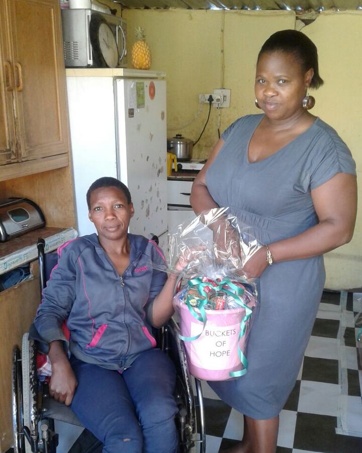A social worker delivering a food parcel to a woman using a wheelchair in her kitchen